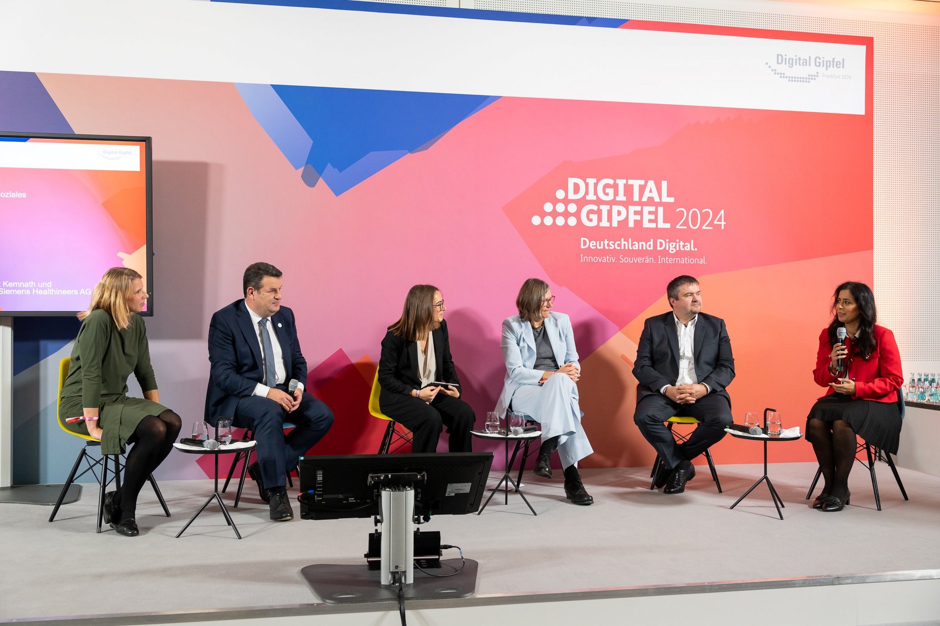 Zu sehen ist ein Podium mit sechs Personen, die auf einer Bühne vor einer Plakatwand mit dem Logo des Digital-Gipfels 2024 sitzen.