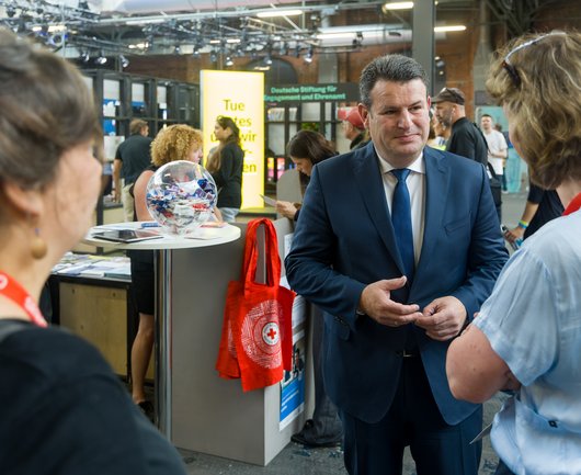 Hubertus Heil, Bundesminister für Arbeit und Soziales, spricht mit zwei Teilnehmer*innen der Veranstaltung. Im Hintergrund schauen weitere Besucher*innen auf die Auslage der Stände.