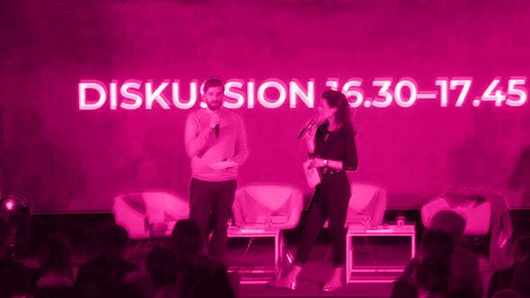 Zwei Personen auf einer Bühne, das Bild ist Pink eingefärbt